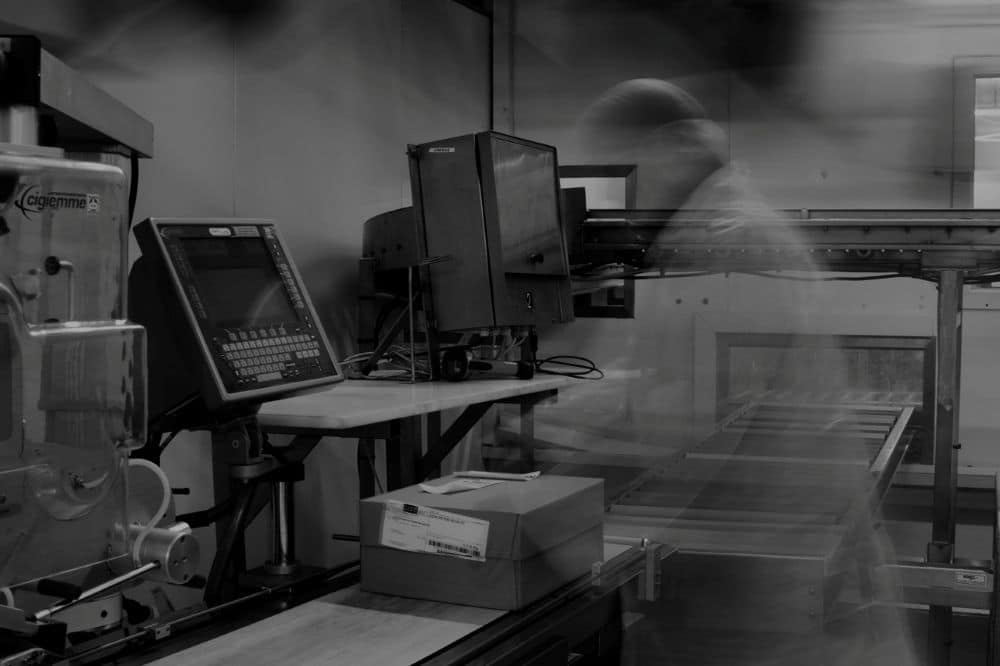 Machine et poste informatique dans une zone de production ou d’impression, avec un opérateur flou en arrière-plan.